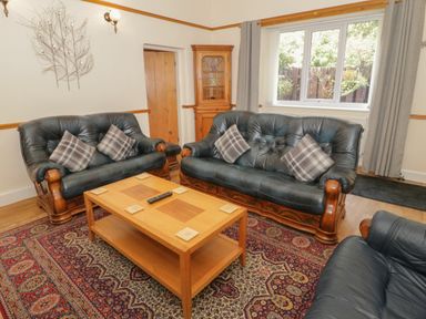 A living room with black leather sofas a wooden coffee table and a patterned carpet at Bangor Cottage in Bangor