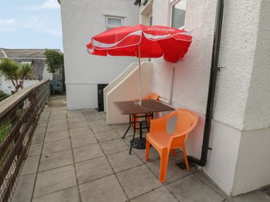 An outdoor patio with a small table under a red Coca Cola umbrella and two orange chairs at Bangor Cottage in Bangor