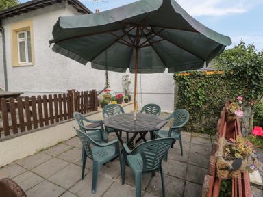 An outdoor patio area with a table and six chairs under a large umbrella surrounded by plants and a wooden fence at Bangor Cottage in Bangor