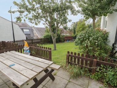 A garden with a wooden picnic table a garden gnome a tree and a bench at Bangor Cottage in Bangor