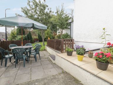 A patio area with a table chairs and an umbrella next to a garden with trees and flowers at Bangor Cottage in Bangor