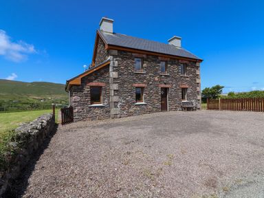 A stone house with multiple windows and chimneys surrounded by grass and hills at Brandon Holiday Home in Cloghane County Kerry