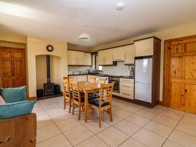 A kitchen and dining area with wooden table and six chairs next to fridge and oven at Brandon Holiday Home in Cloghane County Kerry