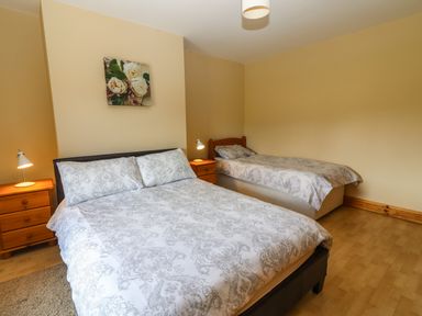 A bedroom with a double bed and a single bed with bedside tables and lamps at Brandon Holiday Home in Cloghane County Kerry