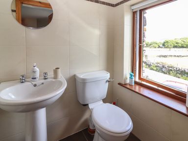 A bathroom with a sink, toilet, round mirror, and window showing an outside view at Brandon Holiday Home in Cloghane County Kerry
