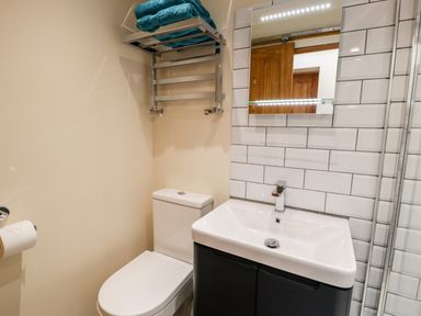 A bathroom with a toilet, a sink with cabinet, a mirror, and a wall-mounted towel rack with towels at Ty Taid Llanddaniel Fab near Beaumaris