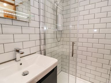 A bathroom with a white sink and faucet next to a glass-enclosed shower with a white tiled wall at Ty Taid in Llanddaniel Fab near Beaumaris