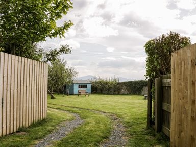 A garden with a gravel path a wooden bench and a blue shed enclosed by wooden fences and hedges at Ty Taid in Llanddaniel Fab near Beaumaris