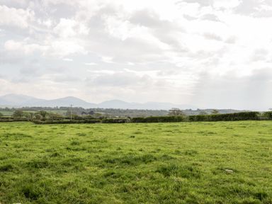 A green grassy field with hedgerows and distant hills under a cloudy sky at Ty Taid in Llanddaniel Fab near Beaumaris