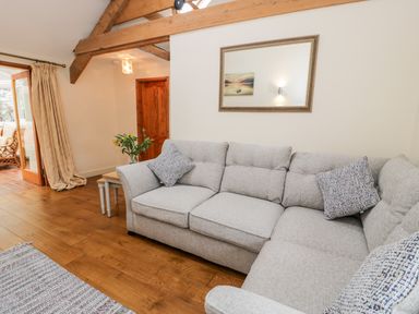 A living room with a gray sofa wooden floor a wooden door and exposed ceiling beams at Ty Taid in Llanddaniel Fab near Beaumaris