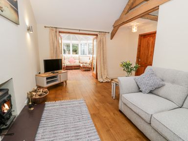 A living room with a gray sofa a TV on a stand a wood burning stove and double doors leading to a sunroom at Ty Taid in Llanddaniel Fab near Beaumaris