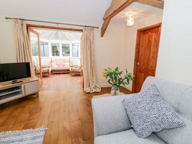 A living room with a gray sofa a patterned cushion flowers on a table and a TV unit with a television at Ty Taid in Llanddaniel Fab near Beaumaris