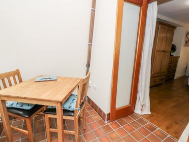 A small wooden dining table with chairs and cushions next to a wooden framed glass door in a room with tiled and wooden flooring at Ty Taid in Llanddaniel Fab near Beaumaris