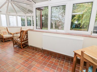 A conservatory with tiled floor wicker chairs and a wooden table at Ty Taid in Llanddaniel Fab near Beaumaris