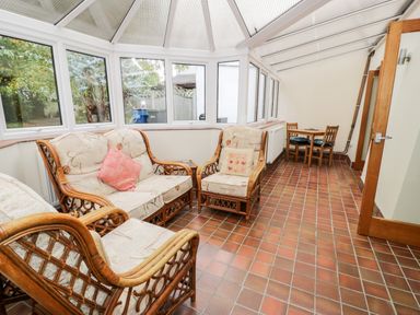 A sunroom with rattan sofa and chairs and a small wooden dining table with chairs at Ty Taid in Llanddaniel Fab near Beaumaris