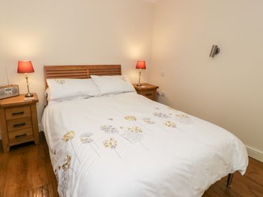 A bedroom with a bed with floral bedding two wooden bedside tables with lamps and a radio at Ty Taid in Llanddaniel Fab near Beaumaris
