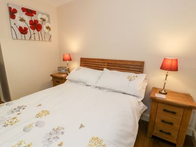 A bedroom with a double bed two bedside tables with lamps and a flower painting on the wall at Ty Taid in Llanddaniel Fab near Beaumaris