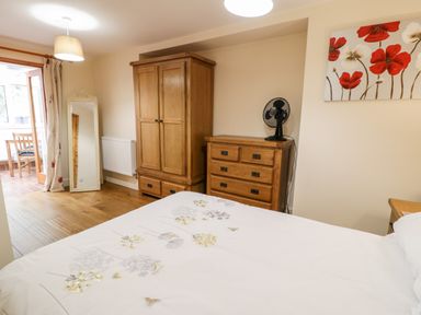 A bedroom with a wooden wardrobe, dresser, standing mirror, bed with floral bedding, and a fan at Ty Taid in Llanddaniel Fab near Beaumaris