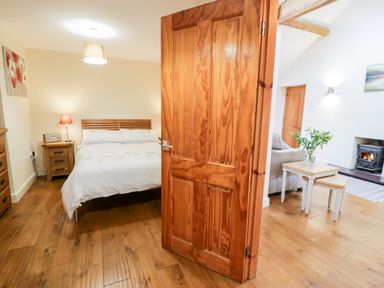 A bedroom with a wooden bed and nightstand next to an open wooden door leading to a living room with tables and a fireplace at Ty Taid in Llanddaniel Fab near Beaumaris