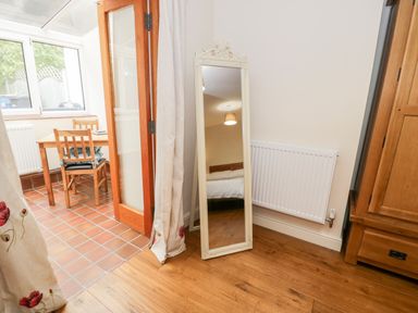 A full length mirror leaning against a wall near a radiator and wooden wardrobe with a view of a dining table and chairs through a doorway at Ty Taid in Llanddaniel Fab near Beaumaris