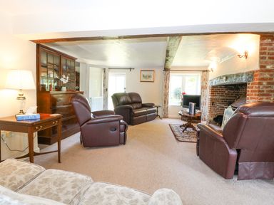 A living room with leather recliners a wooden cabinet a brick fireplace and a small round table with a television at Lyons Green in Little Fransham near Swaffham