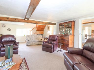 A sitting room with leather chairs a floral sofa wooden cabinet and exposed wooden beams at Lyons Green Little Fransham near Swaffham