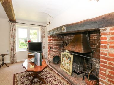 A room with a brick fireplace a wooden coffee table a television and a window with curtains at Lyons Green in Little Fransham near Swaffham