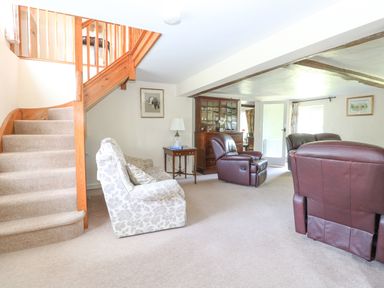 A living room with beige carpet stairs armchairs a wooden cabinet and side table at Lyons Green in Little Fransham near Swaffham