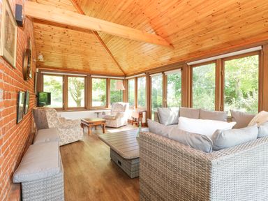 A sunroom with wooden ceiling and windows with wicker and upholstered furniture including armchairs and sofas at Lyons Green in Little Fransham near Swaffham