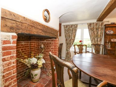 A dining room with a round wooden table wooden chairs floral curtains brick fireplace with flowers in a vase at Lyons Green Little Fransham near Swaffham