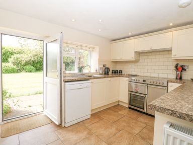 A kitchen with white cabinets a dishwasher a stove an open door leading outside at Lyons Green Little Fransham near Swaffham