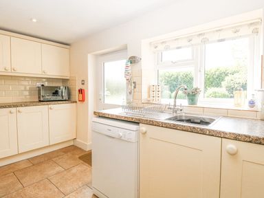 A kitchen with cream cabinets a dishwasher a sink a window and a door at Lyons Green in Little Fransham near Swaffham