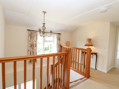 A stair landing with wooden railing a window with curtains a chandelier a side table with a lamp and a decorative vase Lyons Green Little Fransham near Swaffham
