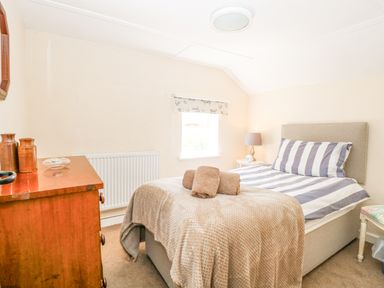 A bedroom with a bed with striped bedding a wooden chest of drawers and a bedside table with a lamp at Lyons Green Little Fransham near Swaffham
