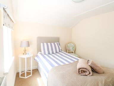 A bedroom with a single bed with striped bedding a bedside table with a lamp and clock and a decorative chair at Lyons Green Little Fransham near Swaffham