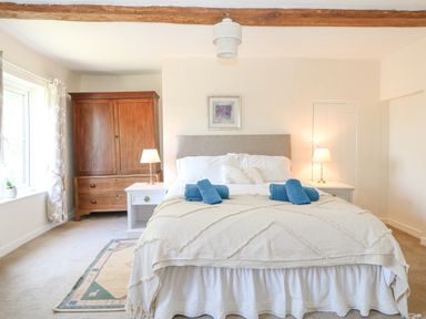A bedroom with a bed with blue towels a wooden wardrobe two bedside tables with lamps and a window at Lyons Green in Little Fransham near Swaffham