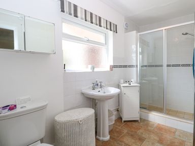 A bathroom with a toilet a wicker laundry basket a pedestal sink a cabinet and a shower with glass doors at Lyons Green in Little Fransham near Swaffham
