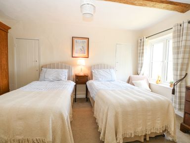 A bedroom with two single beds a wooden nightstand between the beds a window with plaid curtains and a wooden wardrobe at Lyons Green Little Fransham near Swaffham