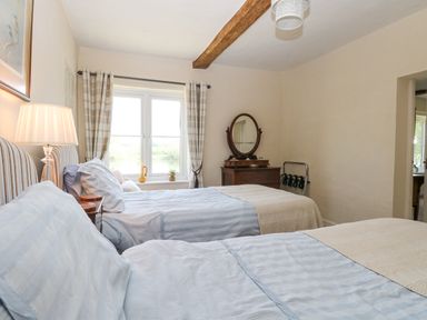 A bedroom with two single beds a window with checkered curtains a wooden dresser with mirror and a lamp at Lyons Green Little Fransham near Swaffham