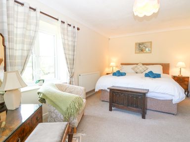 A bedroom with a double bed with two blue towels two bedside tables with lamps a wooden chest at the foot of the bed an armchair with a green blanket a window with curtains and a dresser with a lamp Lyons Green Little Fransham near Swaffham