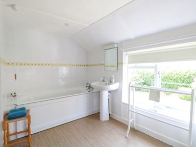 A bathroom with a bathtub sink mirror stool with towels and window with blind at Lyons Green Little Fransham near Swaffham