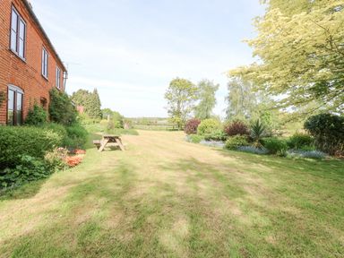 Garden area with lawn and picnic table next to a brick house at Lyons Green in Little Fransham near Swaffham