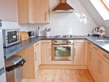 A kitchen with wooden cabinets a stove oven microwave kettle and a cupboard with cups at Suil Na Mara in Aultbea