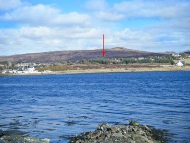 A body of water with rocky shore and houses across the water at Suil Na Mara in Aultbea