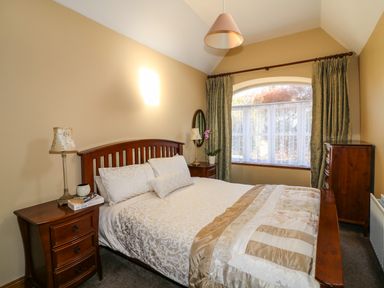 A bedroom with a bed a nightstand with a lamp and books a window with curtains and a wooden dresser at Rosemount Coach House Ballycarney near Enniscorthy County Wexford