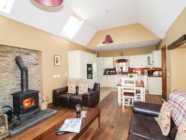 An open living room and kitchen with wood stove and brown leather sofas at Rosemount Coach House Ballycarney near Enniscorthy County Wexford