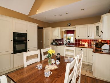 A kitchen with white cabinets wooden dining table and chairs with mugs and scones at Rosemount Coach House Ballycarney near Enniscorthy County Wexford