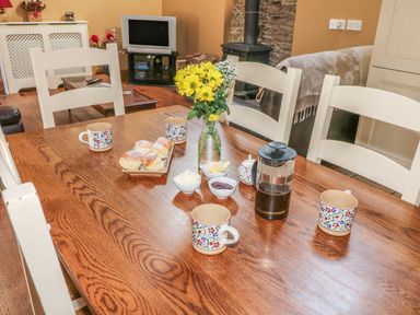 A wooden dining table set with mugs, scones, a French press, butter, jam, cream, and a vase of yellow flowers at Rosemount Coach House Ballycarney near Enniscorthy County Wexford