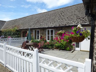 A stone cottage patio with a wooden table and chairs white fencing and hanging flower baskets at Rosemount Coach House in Ballycarney near Enniscorthy County Wexford