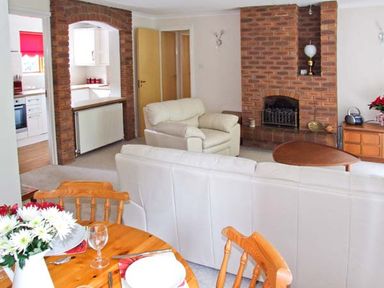 A living room with white sofas a wooden dining table with chairs and a brick fireplace at 9 Bancroft Place in Stratford-upon-Avon